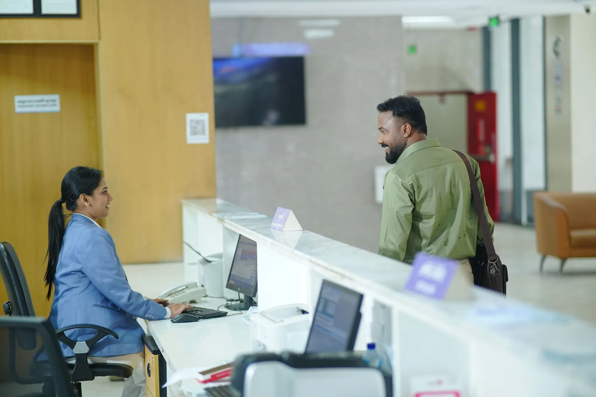A public servant at a service counter computer, with a visitor at the desk