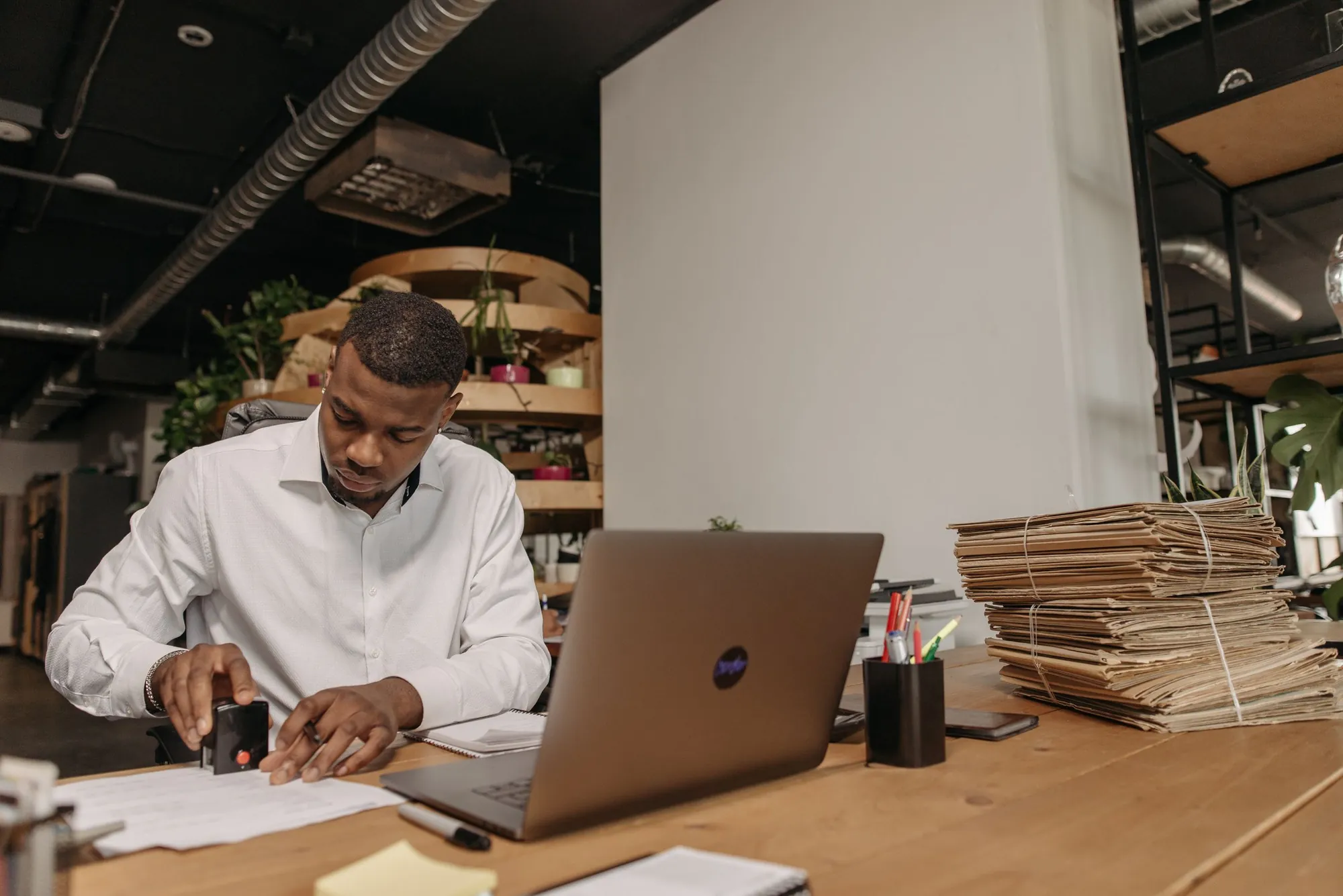 An official stamping a document at his desk, a laptop and bundled files beside him